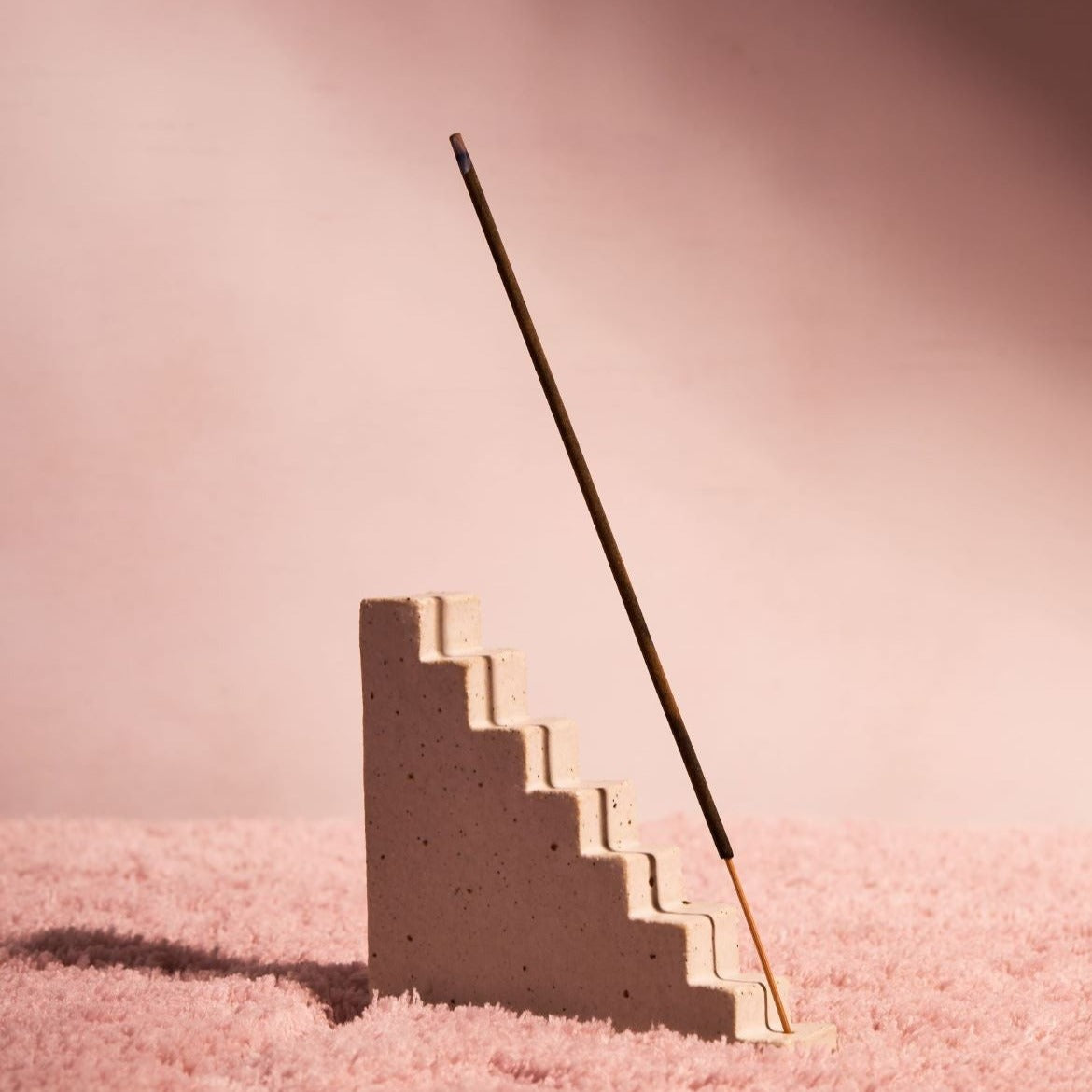 Staircase incense holder with an incense stick coming from the base step and casting a shadow on the stairs.