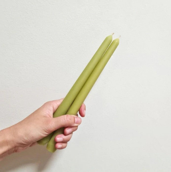 A hand holds two green beeswax candles stocked by Oh Hey Grace