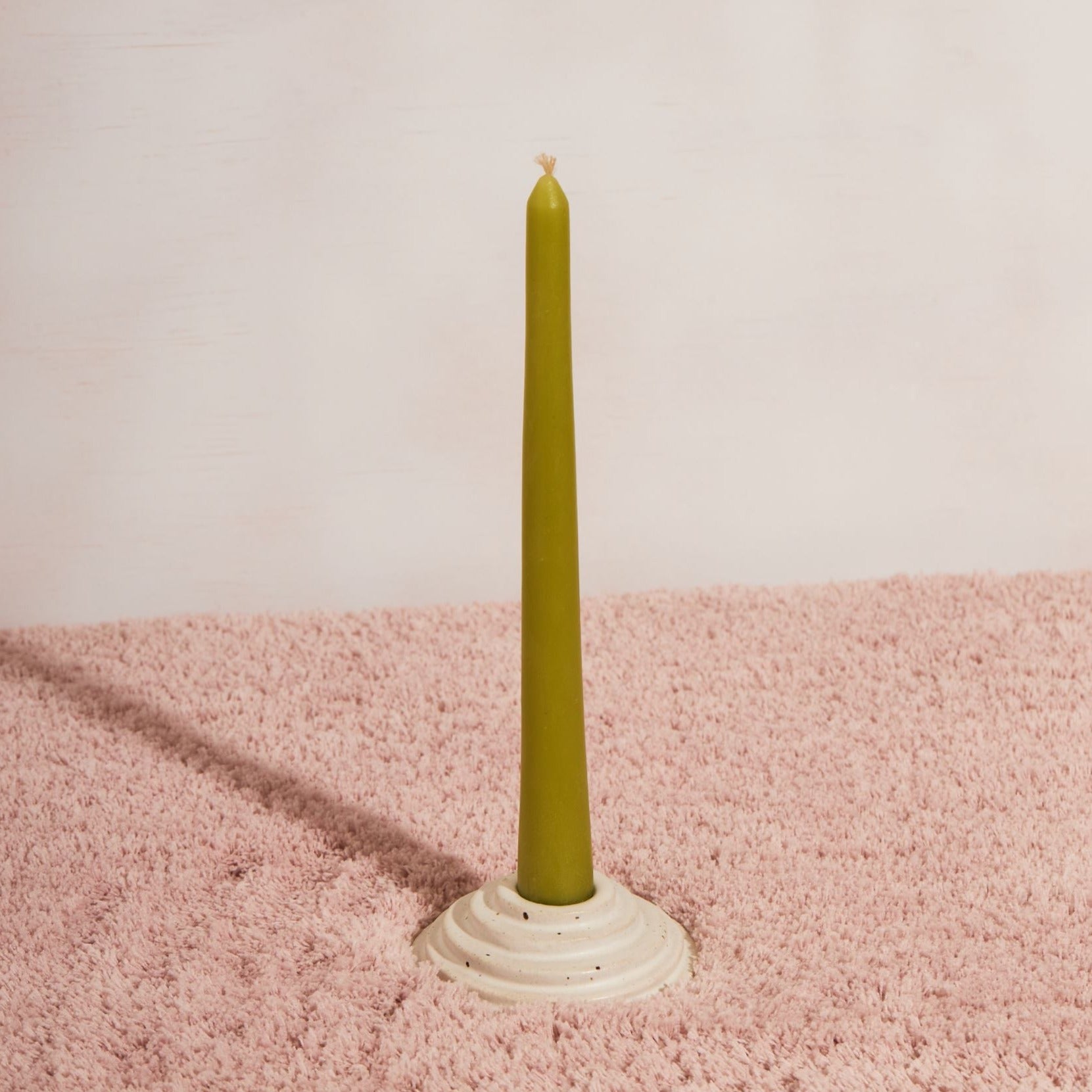 A circular ceramic candle holder featuring steps leading up to the candle. This candle holder has a green unlit candle and is sitting on a pink fluffy fabric with a white backdrop. 