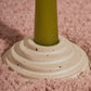 A close up of a circular ceramic candle holder featuring steps leading up to the candle. This candle holder has a green candle and is sitting on a pink fluffy fabric