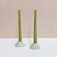 Two circular ceramic candle holders in speckled cream glaze.  Each candle features steps leading up to the candle. Both of the candle holders have green unlit candles and are sitting on a white and cream backdrop. 