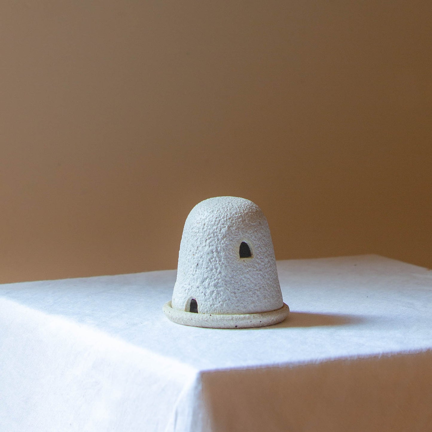 A Dome Burner in lunar glaze sitting on a white plinth. The dome burner has a smooth dome top with hand carved windows and sits on a dish.