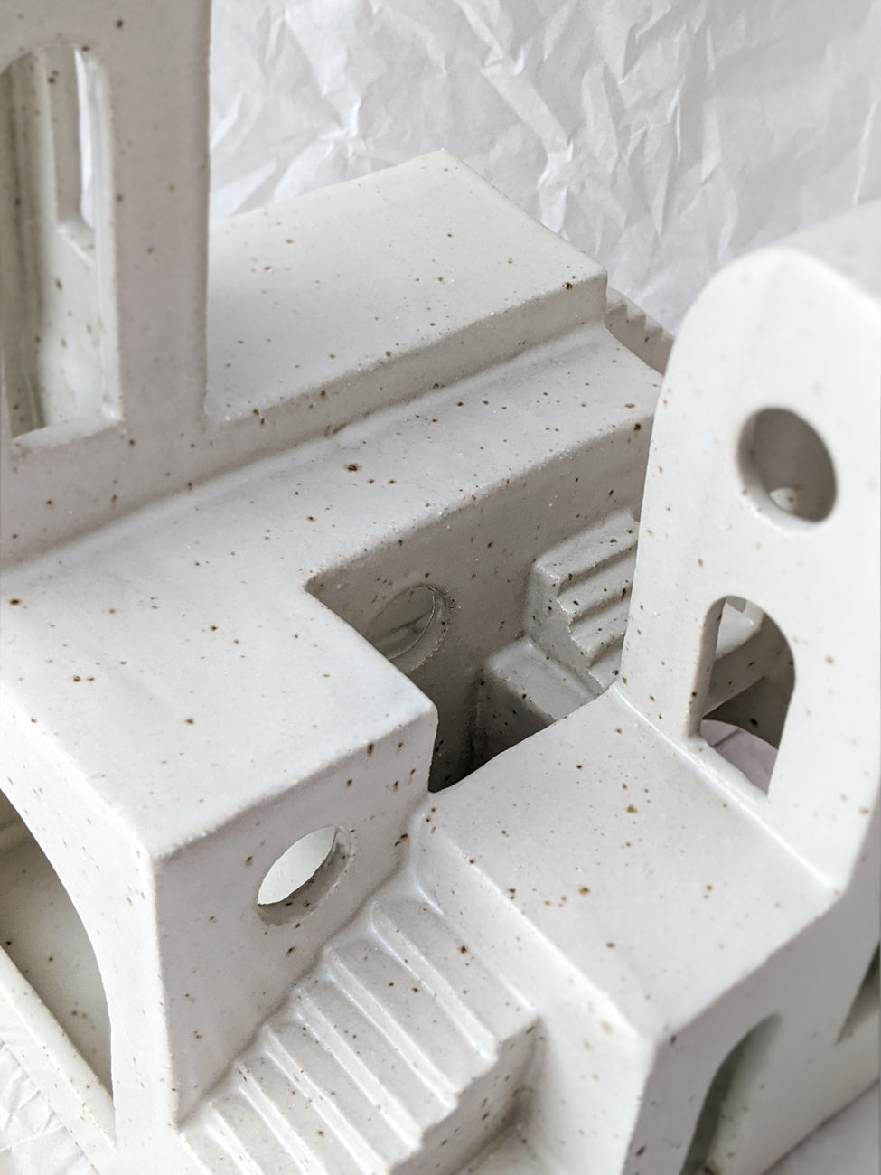 Close up detail of a handmade ceramic sculpture with windows and staircases in speckled cream glaze