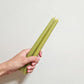 A hand holds two green beeswax candles stocked by Oh Hey Grace 